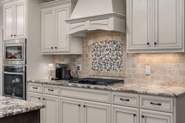 kitchen featuring tasteful backsplash, appliances with stainless steel finishes, light stone countertops, and custom exhaust hood