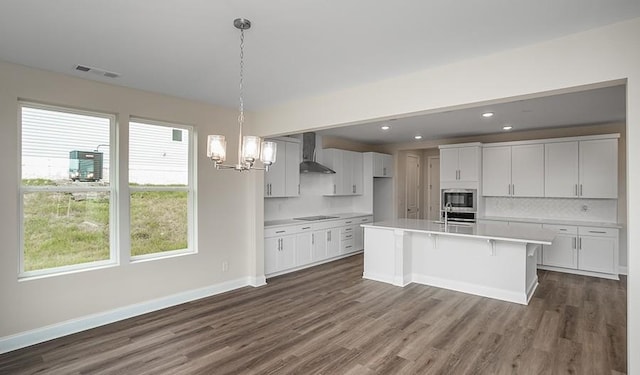 kitchen featuring wall chimney exhaust hood, white cabinetry, decorative light fixtures, a center island, and stainless steel microwave