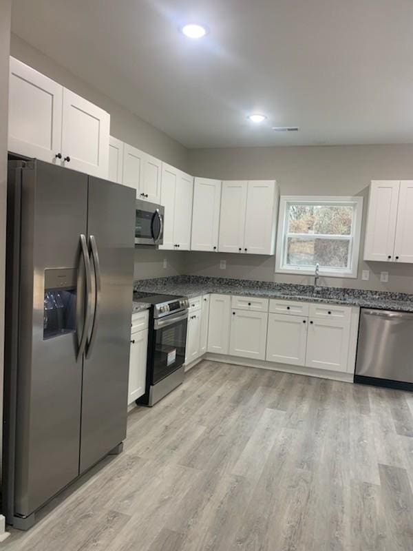 kitchen featuring dark stone countertops, stainless steel appliances, light hardwood / wood-style floors, and white cabinets