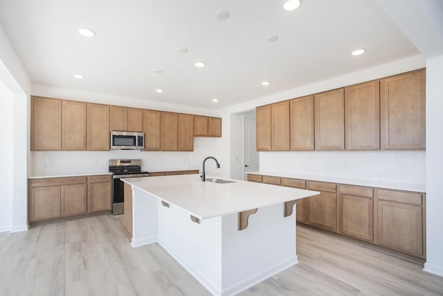 kitchen with a kitchen bar, sink, light wood-type flooring, an island with sink, and stainless steel appliances