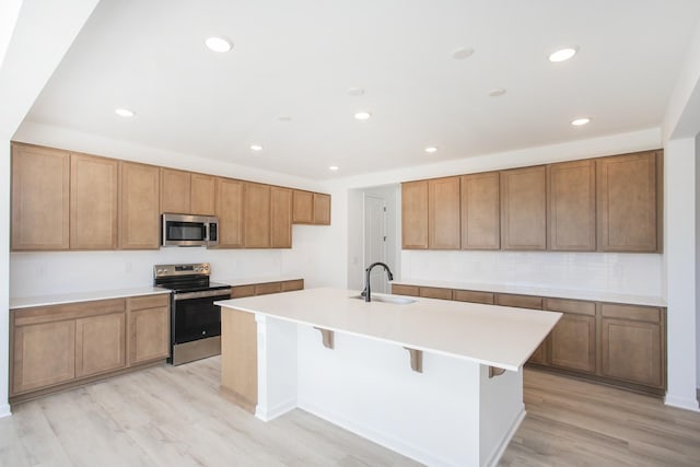 kitchen featuring stainless steel appliances, sink, an island with sink, and light hardwood / wood-style flooring