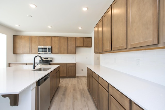 kitchen with backsplash, appliances with stainless steel finishes, sink, and light wood-type flooring