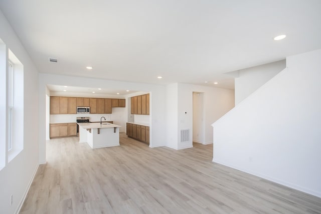 kitchen featuring sink, a breakfast bar area, a kitchen island with sink, stainless steel appliances, and light wood-type flooring