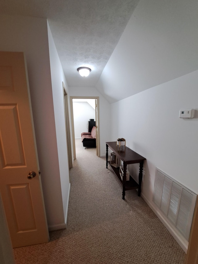 hallway featuring lofted ceiling, light colored carpet, and a textured ceiling