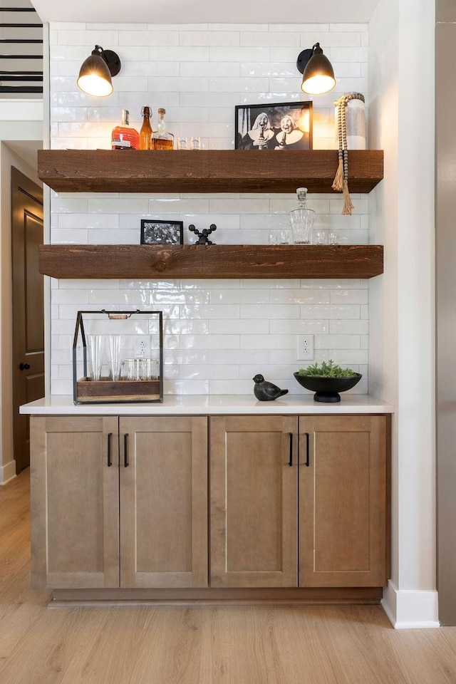 bar with tasteful backsplash and light hardwood / wood-style flooring