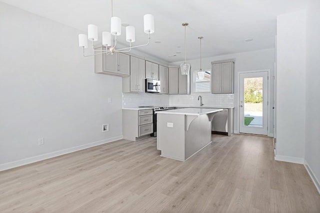 kitchen featuring gray cabinetry, appliances with stainless steel finishes, a kitchen island, pendant lighting, and decorative backsplash