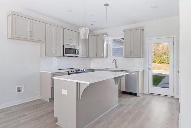 kitchen featuring appliances with stainless steel finishes, pendant lighting, gray cabinetry, a center island, and light wood-type flooring