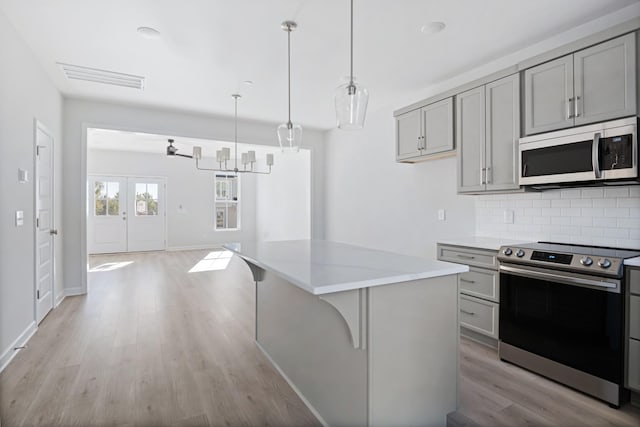 kitchen featuring tasteful backsplash, appliances with stainless steel finishes, gray cabinets, a kitchen island, and pendant lighting