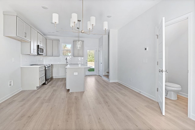 kitchen with decorative light fixtures, light hardwood / wood-style flooring, a center island, and appliances with stainless steel finishes