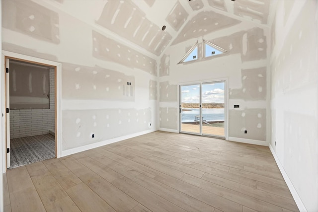 unfurnished room with a water view, light hardwood / wood-style floors, and high vaulted ceiling