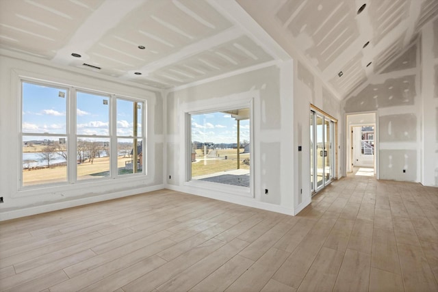 empty room with a water view, high vaulted ceiling, and light hardwood / wood-style flooring