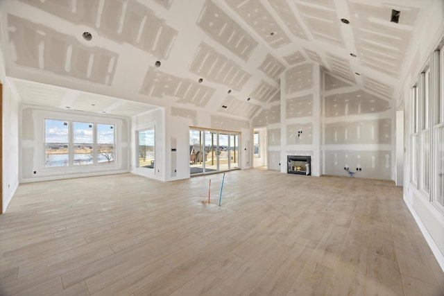 unfurnished living room featuring high vaulted ceiling and light hardwood / wood-style floors