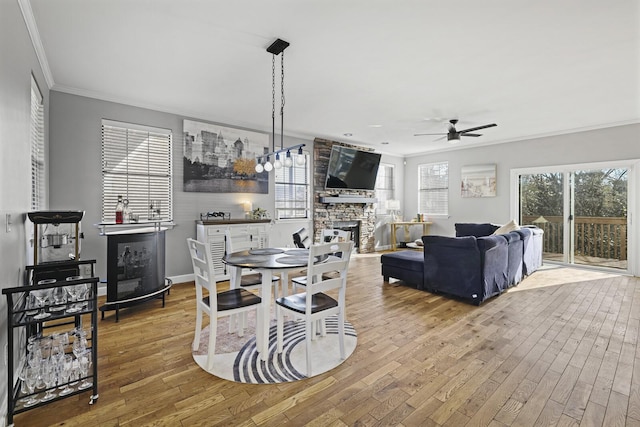 dining area featuring crown molding, a stone fireplace, a wealth of natural light, and hardwood / wood-style flooring