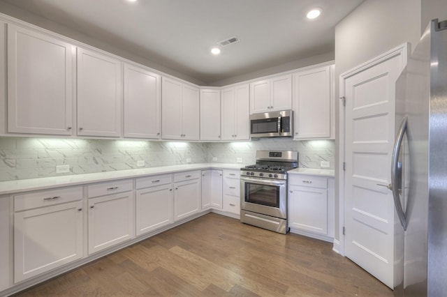 kitchen with stainless steel appliances, white cabinetry, hardwood / wood-style floors, and decorative backsplash