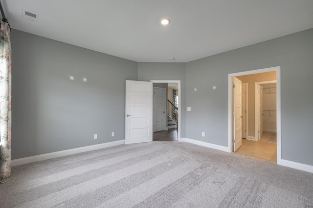 unfurnished bedroom with a walk in closet, light colored carpet, and a closet