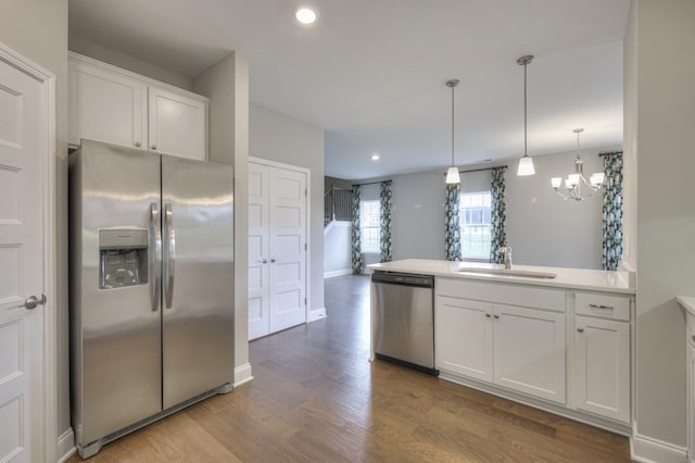 kitchen featuring sink, appliances with stainless steel finishes, white cabinetry, decorative light fixtures, and light wood-type flooring