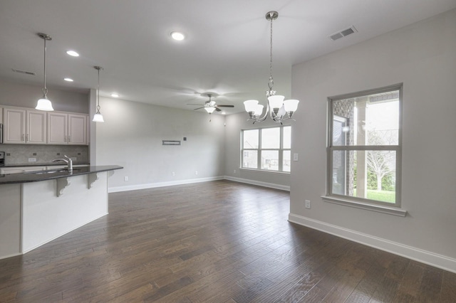 unfurnished living room featuring dark hardwood / wood-style flooring and ceiling fan with notable chandelier