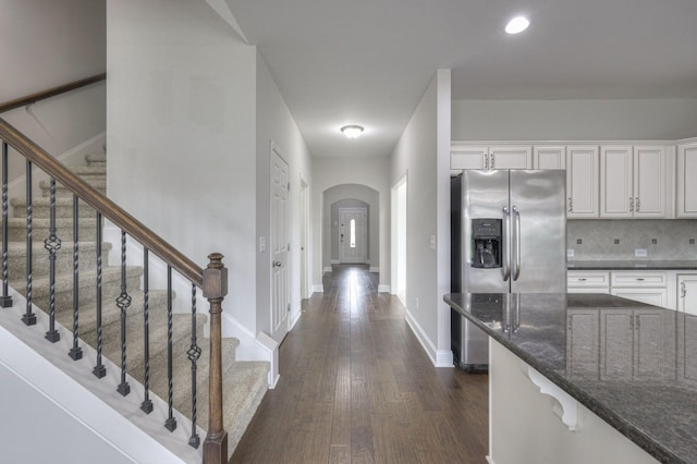 interior space with backsplash, dark hardwood / wood-style floors, stainless steel refrigerator with ice dispenser, white cabinets, and dark stone counters