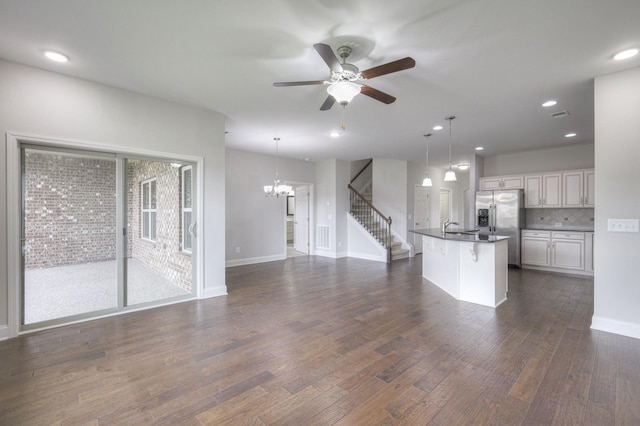 unfurnished living room with dark wood-type flooring, sink, and ceiling fan with notable chandelier