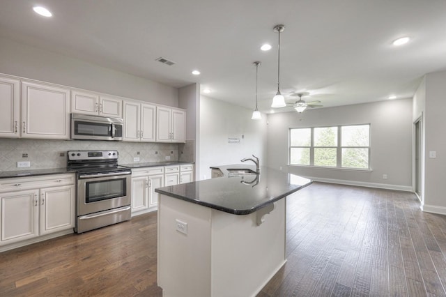 kitchen with white cabinetry, stainless steel appliances, a kitchen island with sink, and decorative backsplash