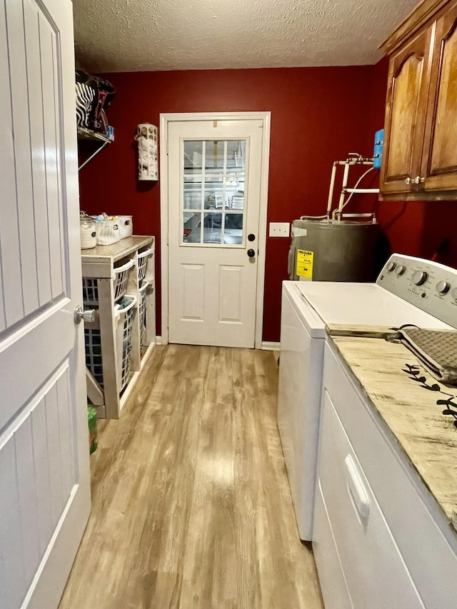 laundry room with washing machine and dryer, cabinets, a textured ceiling, electric water heater, and light hardwood / wood-style floors