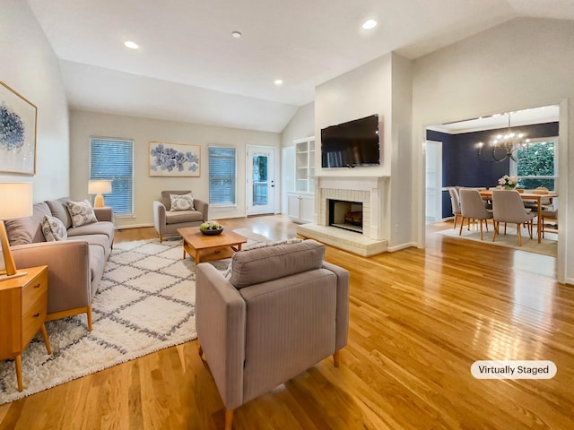 living room with light hardwood / wood-style flooring, a brick fireplace, vaulted ceiling, and a chandelier