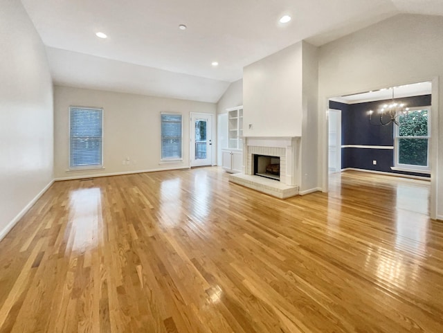 unfurnished living room featuring built in features, a fireplace, lofted ceiling, a notable chandelier, and light wood-type flooring