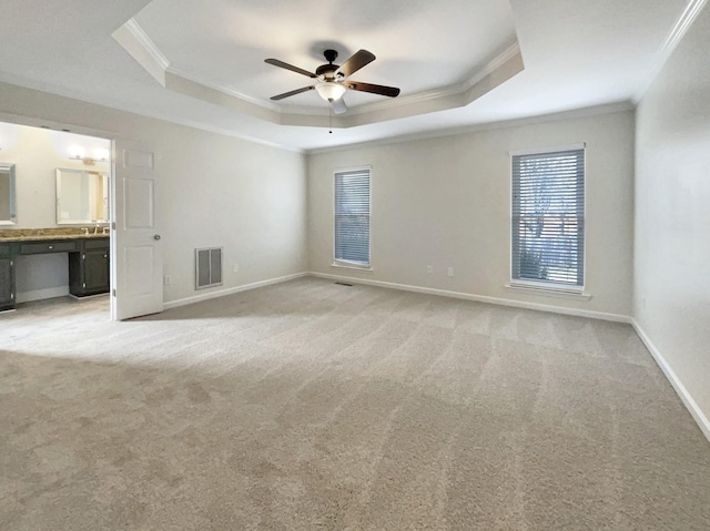 unfurnished bedroom with ensuite bathroom, crown molding, light carpet, a raised ceiling, and ceiling fan