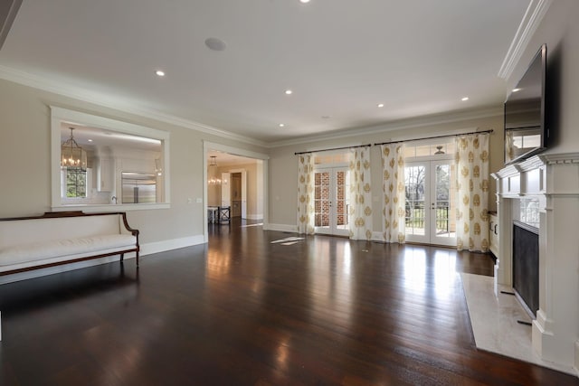 unfurnished living room with dark hardwood / wood-style floors, a fireplace, ornamental molding, an inviting chandelier, and french doors