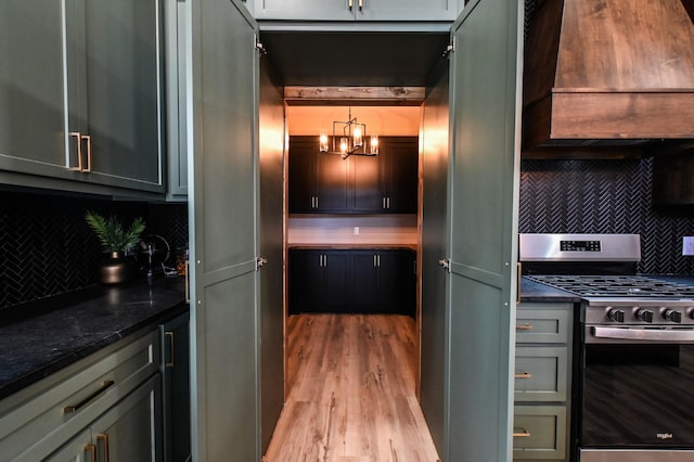 kitchen with premium range hood, gas stove, decorative light fixtures, dark stone counters, and backsplash