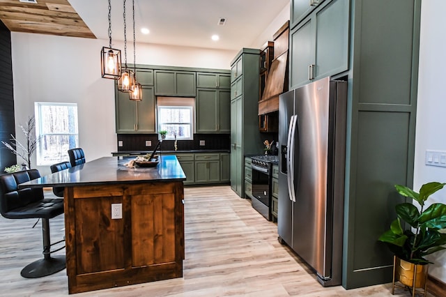 kitchen featuring a breakfast bar, stainless steel appliances, custom range hood, green cabinetry, and decorative light fixtures