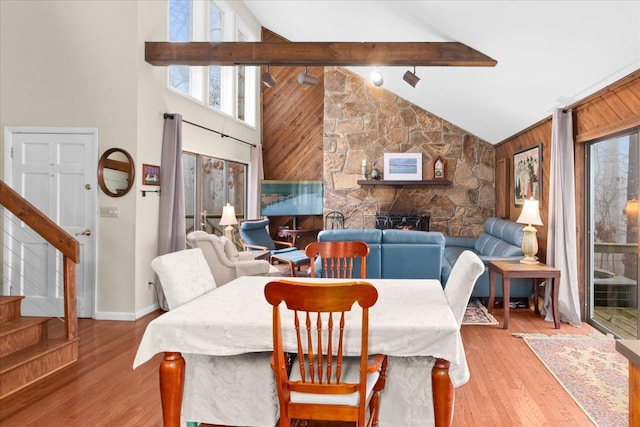 dining area featuring light hardwood / wood-style flooring, wooden walls, high vaulted ceiling, a fireplace, and beamed ceiling