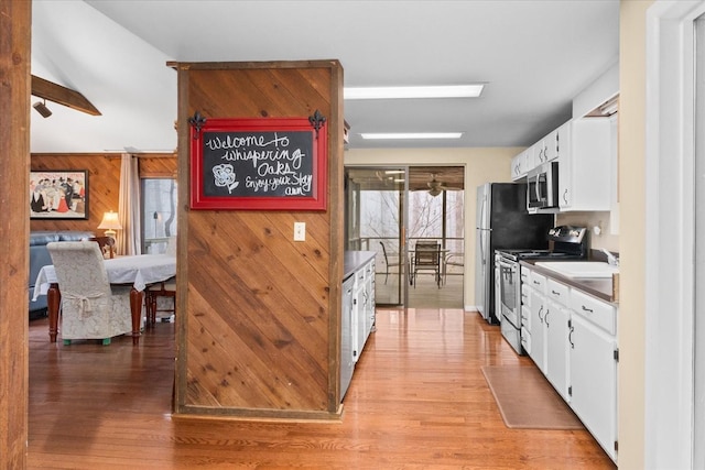 kitchen with appliances with stainless steel finishes, light hardwood / wood-style flooring, white cabinets, and wood walls