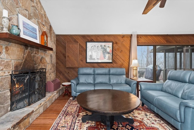 living room with lofted ceiling with beams, wooden walls, a stone fireplace, and hardwood / wood-style floors