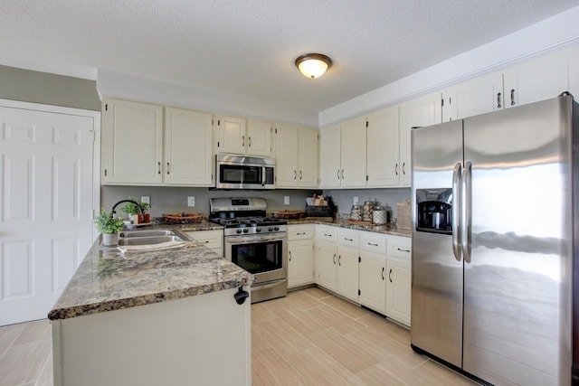 kitchen with appliances with stainless steel finishes, white cabinetry, sink, kitchen peninsula, and a textured ceiling