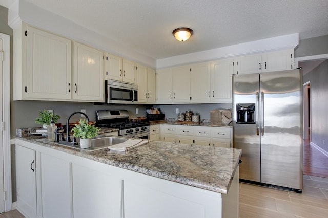 kitchen featuring white cabinetry, sink, dark stone countertops, kitchen peninsula, and stainless steel appliances