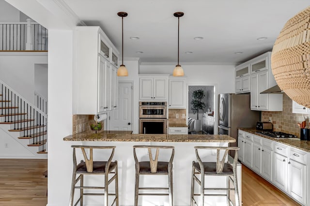 kitchen with dark stone countertops, double oven, white cabinetry, and light wood-type flooring