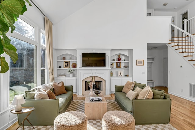 living room featuring built in shelves, light hardwood / wood-style floors, and high vaulted ceiling