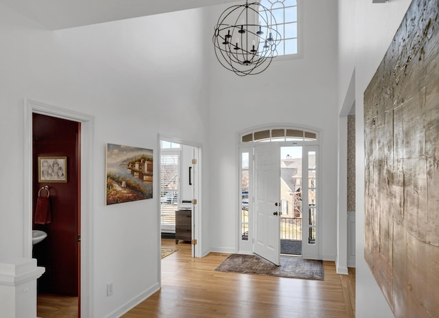 foyer entrance featuring a towering ceiling, an inviting chandelier, and light hardwood / wood-style flooring