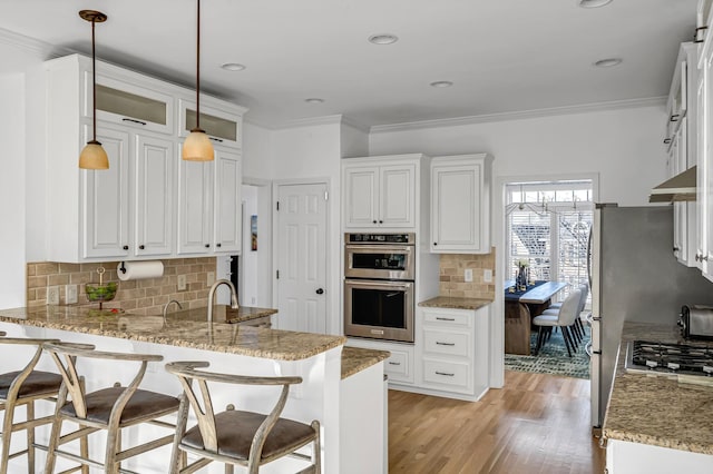 kitchen with stainless steel appliances, white cabinetry, light stone countertops, and pendant lighting