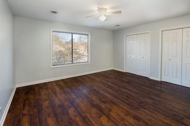 unfurnished bedroom with dark wood-type flooring, ceiling fan, and multiple closets