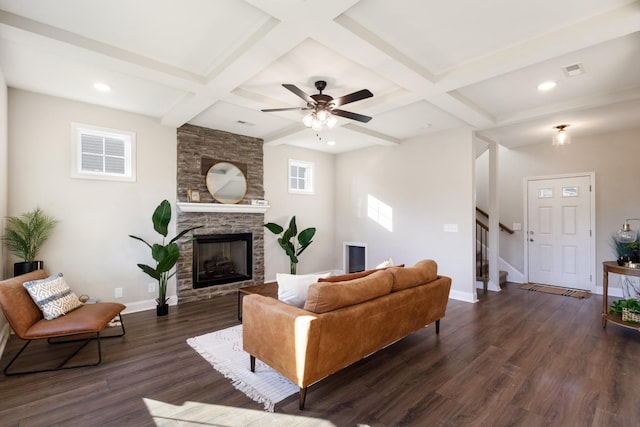 living room featuring dark wood-type flooring, coffered ceiling, a stone fireplace, beamed ceiling, and ceiling fan