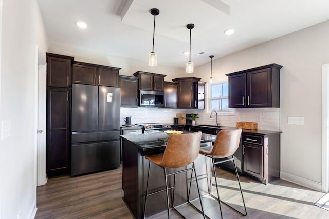 kitchen with appliances with stainless steel finishes, dark hardwood / wood-style floors, decorative light fixtures, sink, and a center island