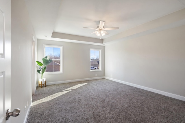 empty room featuring ceiling fan, a raised ceiling, carpet, and a wealth of natural light