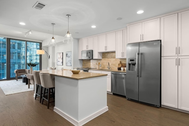 kitchen with white cabinetry, stainless steel appliances, decorative light fixtures, and a kitchen island