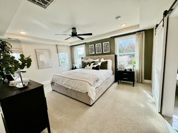 bedroom with a barn door, ceiling fan, and a tray ceiling