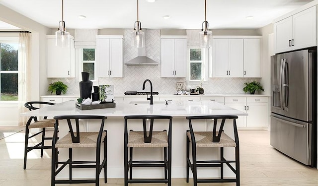 kitchen with stainless steel appliances, pendant lighting, a kitchen island with sink, and wall chimney range hood