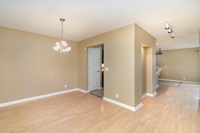 unfurnished room featuring an inviting chandelier, light hardwood / wood-style flooring, rail lighting, and a textured ceiling