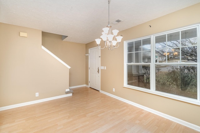 unfurnished dining area featuring a chandelier, a textured ceiling, and light hardwood / wood-style flooring