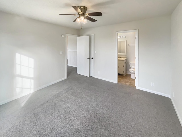 unfurnished bedroom featuring ceiling fan, ensuite bath, and dark colored carpet